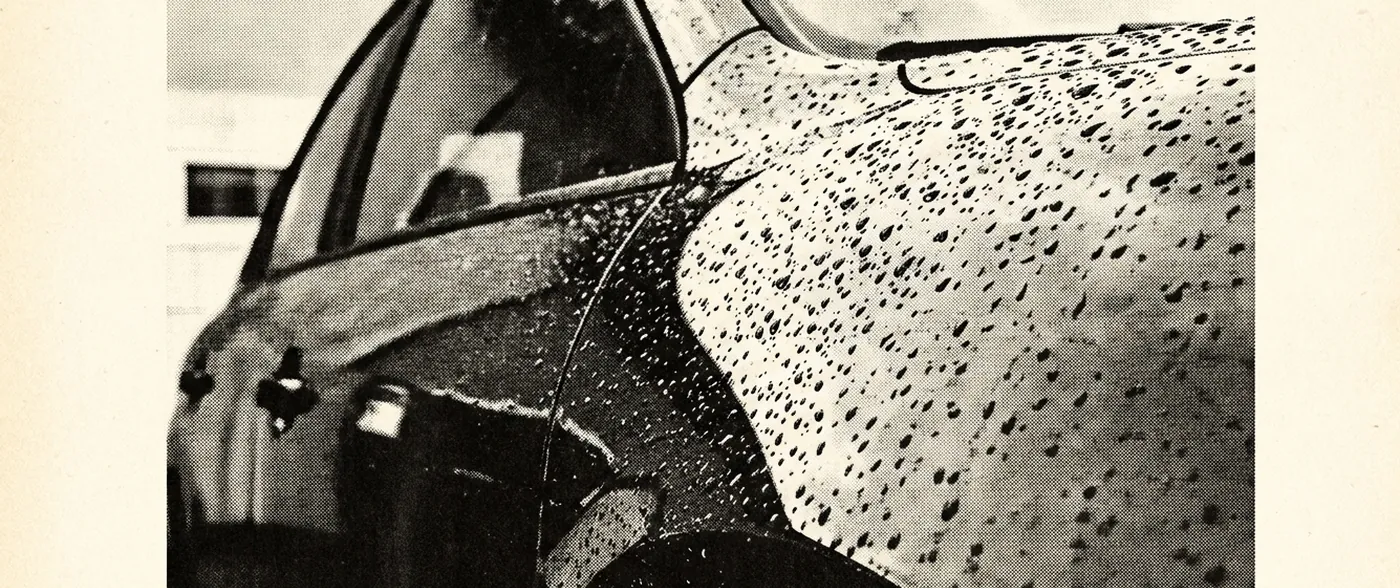 A close view across the wet, curved flank of a car body panel with water beaded across deep gloss.